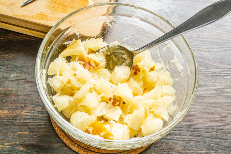 Gently tossing the fruit salad to coat everything in the dressing A bowl of fruit salad with pomelo and pear being gently mixed with the dressing.