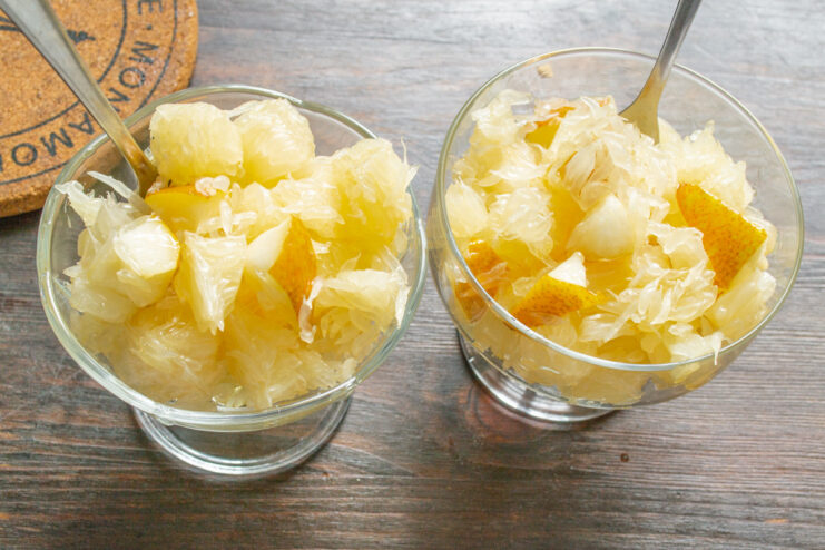 Serving the pomelo fruit salad in elegant glass bowls The pomelo and pear fruit salad being spooned into individual glass serving bowls.
