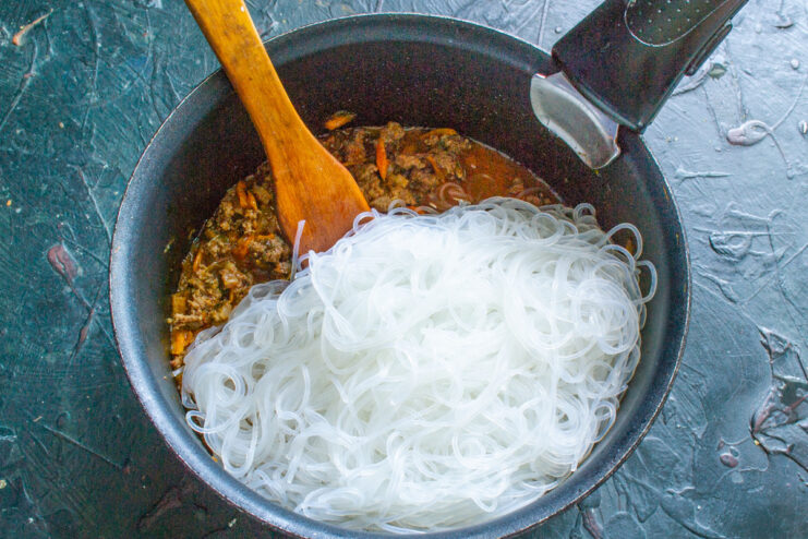 Combining Noodles and Sauce - Tossing everything together. Cooked funchoza noodles being added to the pan with the meat sauce.