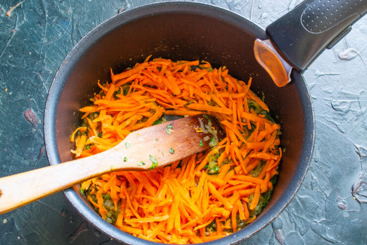 Adding Carrots to the Pan - For sweetness and texture. Grated carrots being added to the pan with other vegetables and spices.