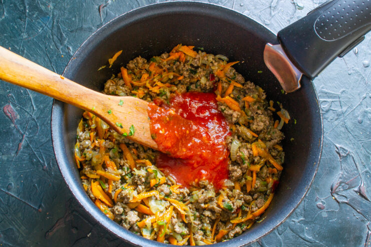 Adding Tomato Purée - To create a rich and savory sauce. Tomato purée being poured into the sauté pan with the cooking ground beef and vegetables.