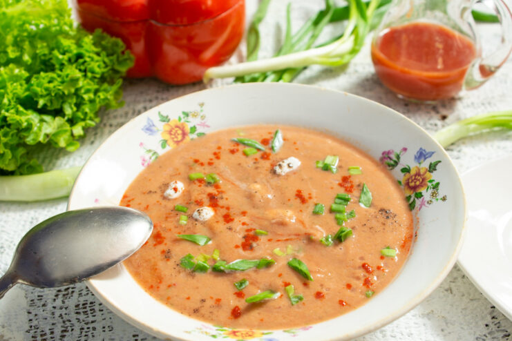 A bowl of bright red Gazpacho, a cold tomato soup, garnished with fresh herbs.