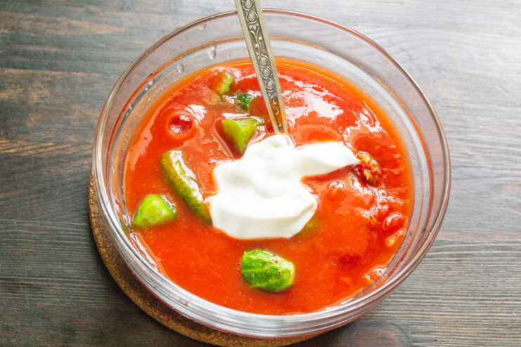A Creamy Twist: Adding Smetana or Yogurt to Gazpacho A spoonful of creamy white smetana (sour cream) being added to the gazpacho mixture.