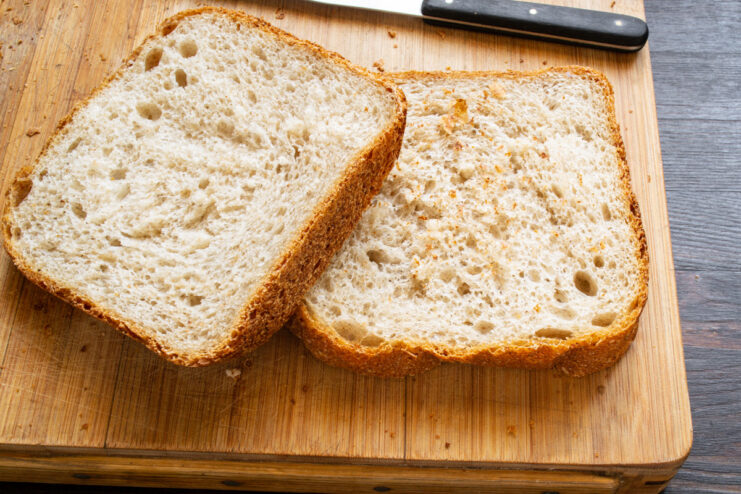How to Prepare Bread for Savory French Toast Sandwiches A person cutting thick slices of white wheat bread on a wooden board.
