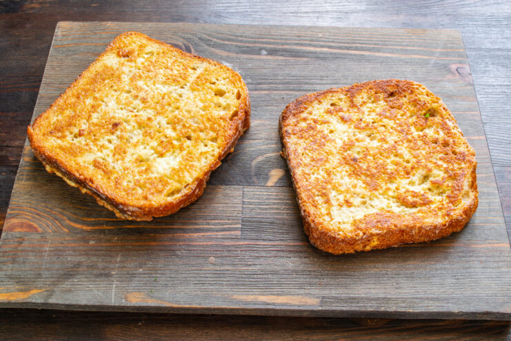 Frying the Egg-Soaked Bread to a Perfect Golden Brown Two slices of egg-battered bread frying in a pan until golden brown.