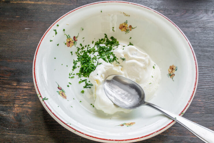 Making the Creamy Cheese and Herb Spread for the Sandwich A bowl with cream cheese, sour cream, and chopped parsley being mixed.