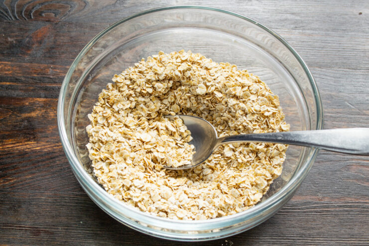 Step 1: Adding Rolled Oats to a Mixing Bowl A person pouring rolled oats from a container into a glass mixing bowl.