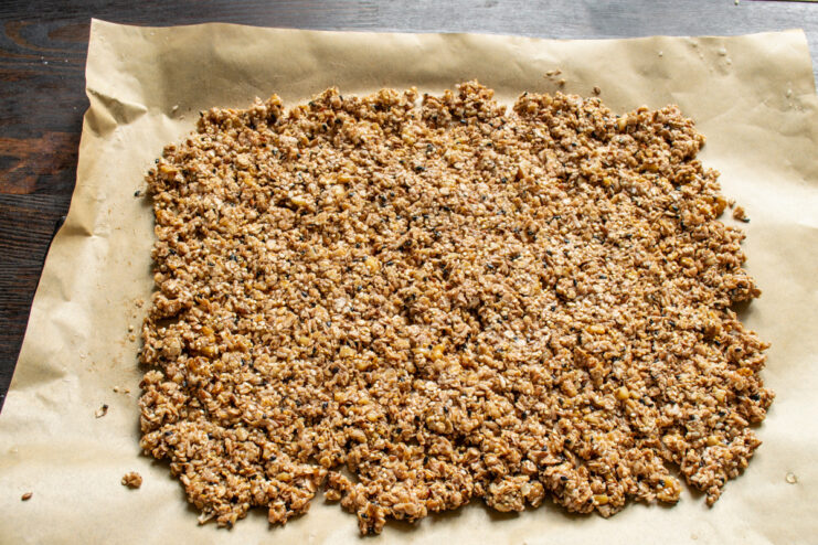 Pressing the Granola into an Even Layer for Baking Using a spatula to press the granola mixture into a thin, even layer on the baking sheet.