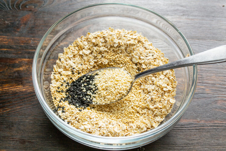 Mixing in Black and White Sesame Seeds Sprinkling a mix of black and white sesame seeds into the granola mixture.