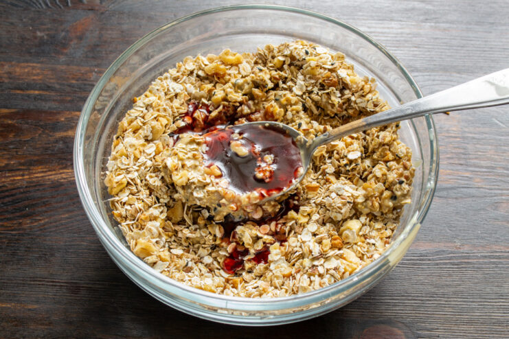 Sweetening Naturally with Rosehip Syrup Pouring rosehip syrup over the dry granola ingredients.