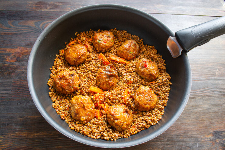 Seared meatballs being arranged on top of the layer of buckwheat in a pan.