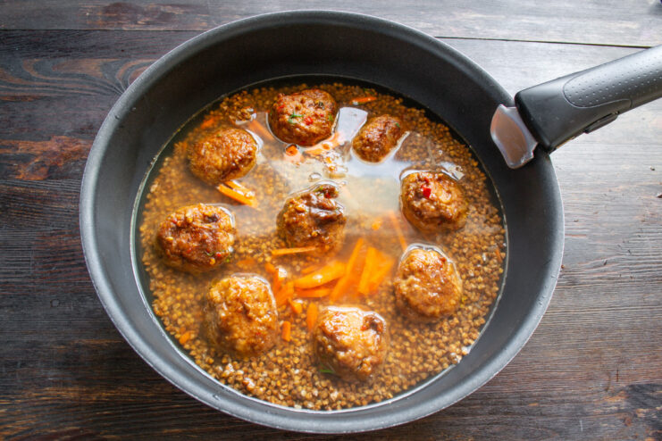 Pouring water into the pan with buckwheat and meatballs before baking.
