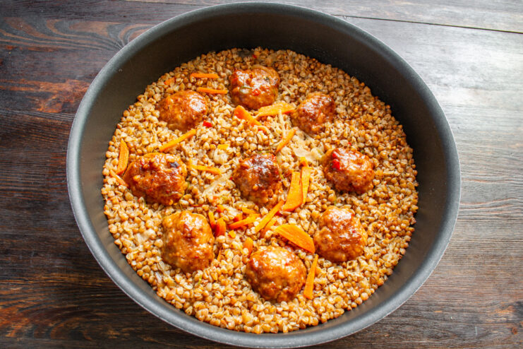 The finished dish of baked buckwheat with meatballs, covered with a kitchen towel to rest.