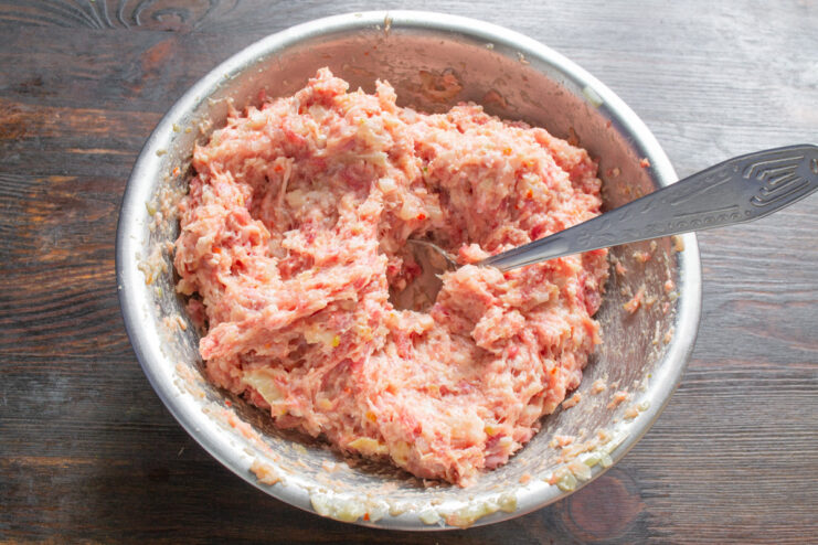 Hands mixing the ground meat mixture in a bowl to prepare the meatballs.