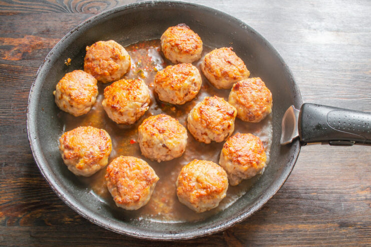 Raw, perfectly shaped meatballs lined up on a surface before cooking.