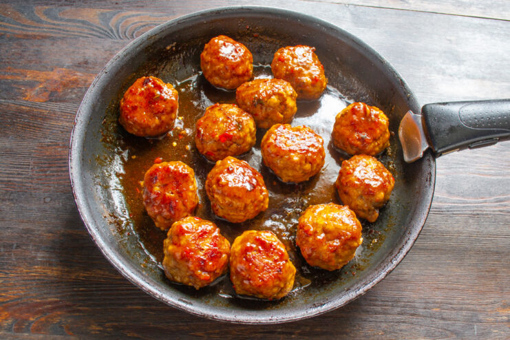 Pouring soy sauce over pan-seared meatballs in a frying pan.
