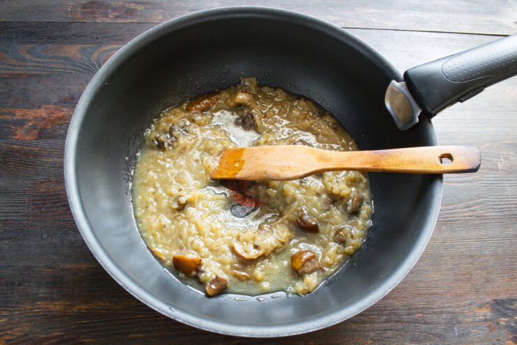 Adding chopped mushrooms to a pan of sautéed onions.
