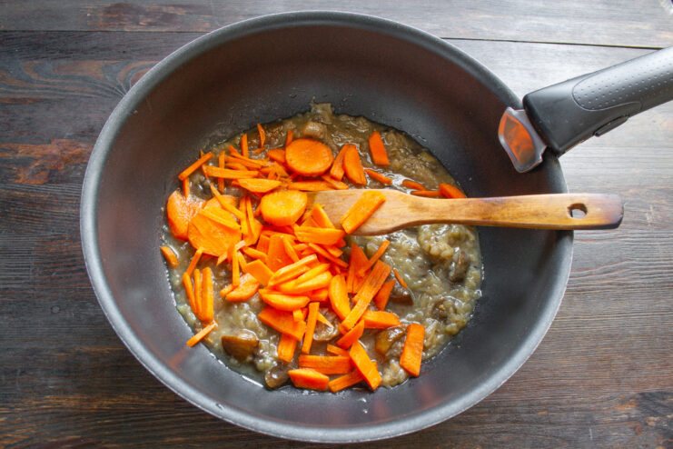 Carrots being cut into thin strips (julienned) on a cutting board.
