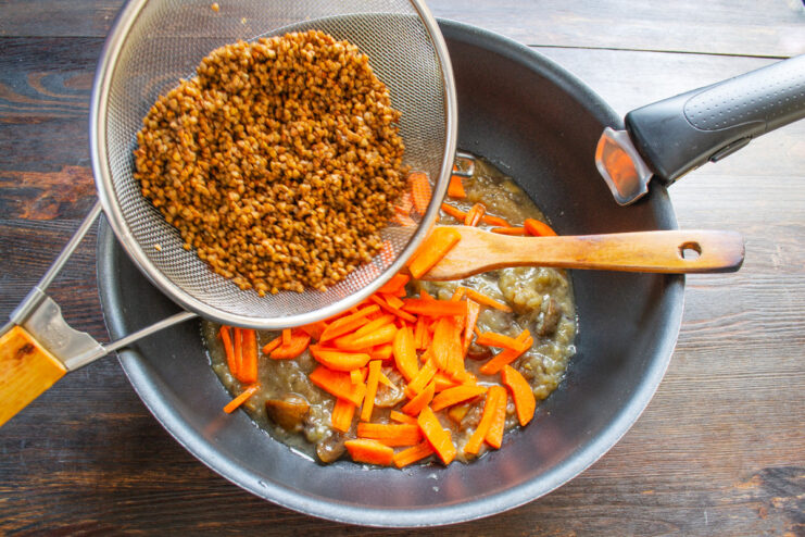 Pouring rinsed buckwheat groats into a pan with sautéed vegetables.