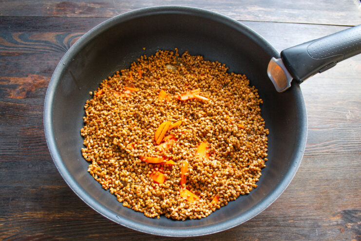 Buckwheat spread in an even layer in a pan over a bed of vegetables.