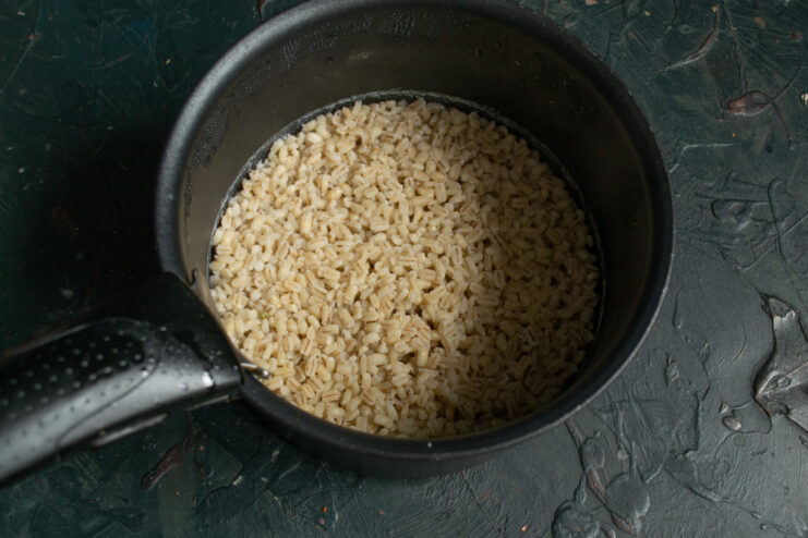 Draining the pearl barley to get the perfect consistency for the soup. Cooked pearl barley being drained in a metal sieve over a sink.