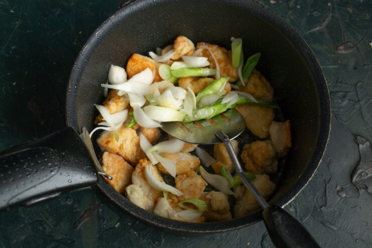 Adding onions to the seared chicken to build the soup's flavor base. Chopped onions being added to the pot with golden-brown chicken pieces.