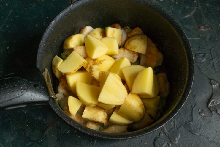 Preparing new potatoes for the rassolnik soup. New potatoes being cut into large chunks on a cutting board.