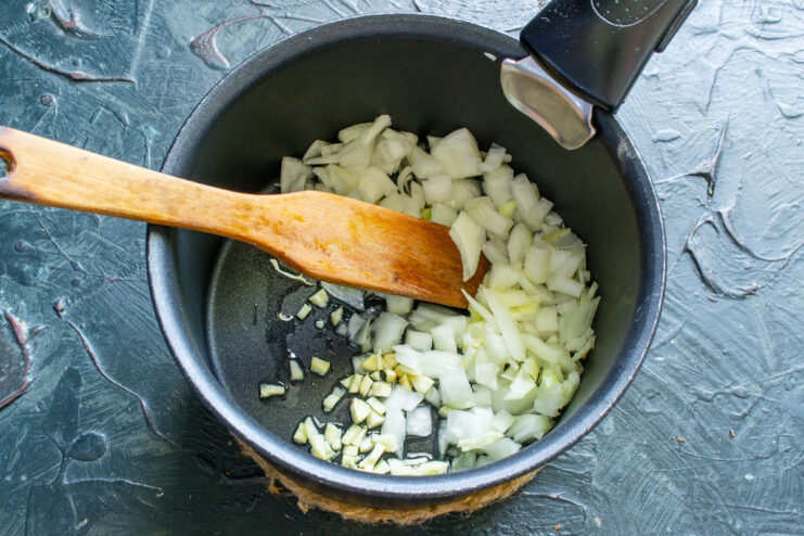 Sautéing Onions and Garlic to Build a Flavor Base Finely chopped onion and garlic being sautéed in a pan to create an aromatic base.