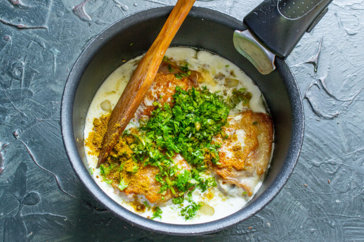 Adding Fresh Herbs and Spices for Authentic Uzbek Flavor Adding chopped cilantro and ground spices to the chicken and sauce in the pan.