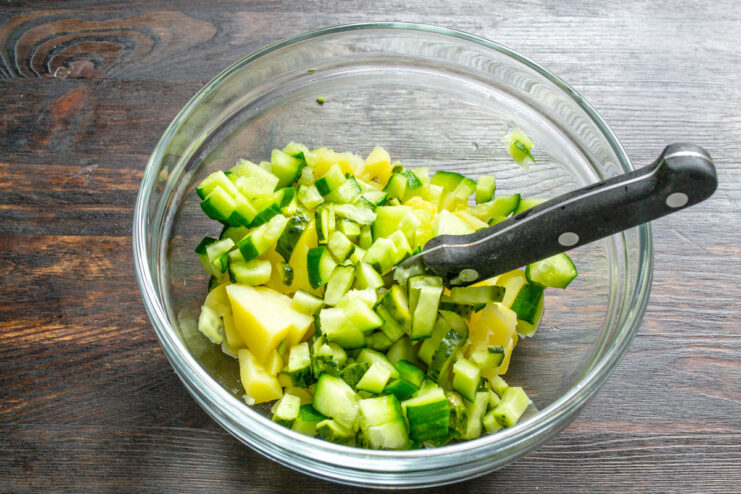Adding crispness: fresh cucumbers join the potatoes. Diced fresh cucumbers being added to a bowl of diced potatoes.