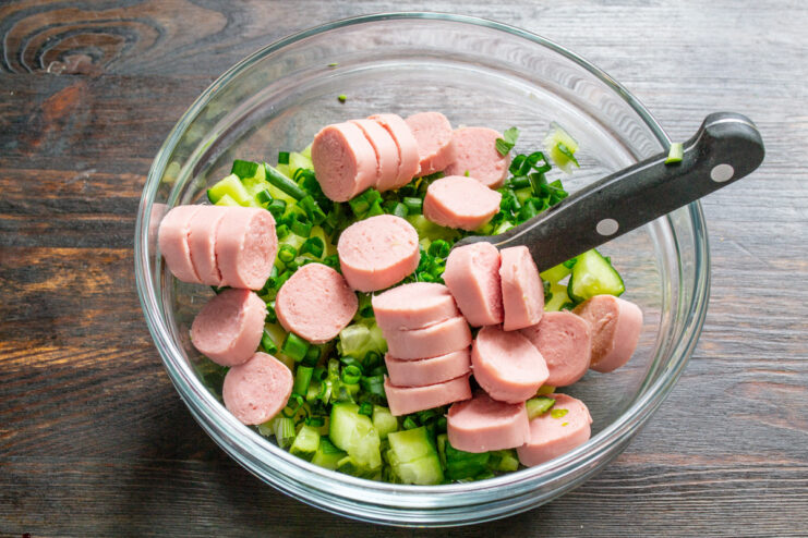 Adding a savory element: slicing Doktorskie sausages. Slicing mild sausages into thin rounds for the Kholodnik soup.