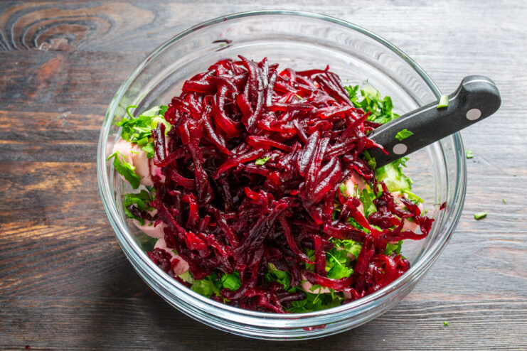 The key to the color: grating a cooked beet into the mix. Grating a cooked red beet into a bowl with other chopped vegetables.