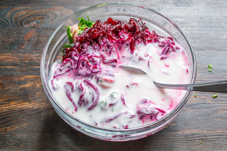 Creating the creamy base by pouring in cold kefir. Pouring cold, white kefir into a bowl of chopped vegetables and sausages.