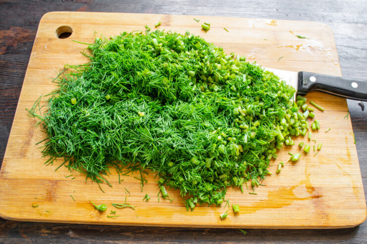 Chopping dill finely to ensure even drying in the oven A pile of finely chopped fresh dill on a cutting board.