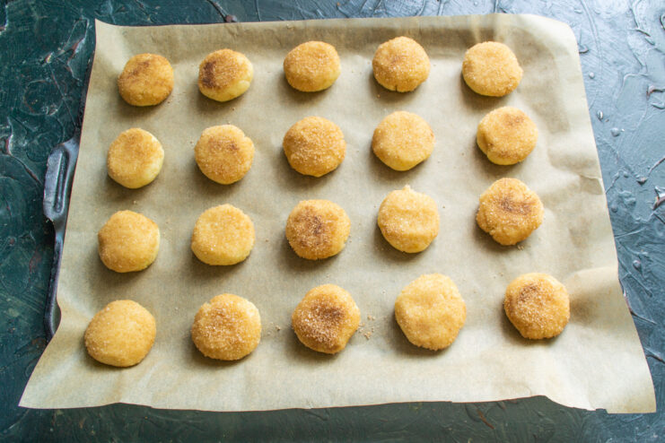 Arranging cookies on a baking sheet before baking Raw cookie dough balls coated in cinnamon sugar arranged on a parchment-lined baking sheet.