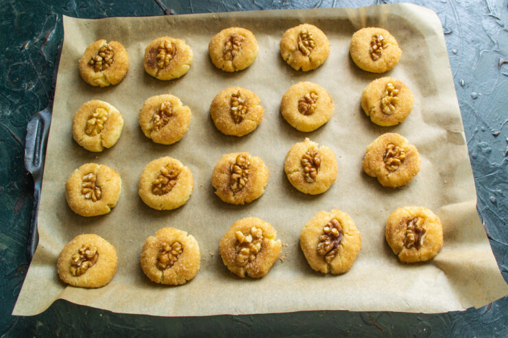 Topping cookies with walnuts before baking A hand pressing a walnut quarter into the top of a raw cookie dough ball.