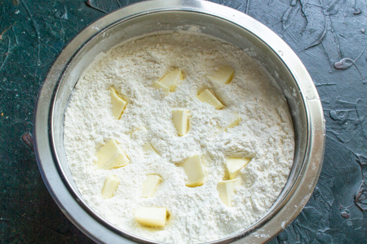 Adding cubed cold butter to the flour mixture Cubes of cold butter being added to the flour and sugar mixture in a bowl.