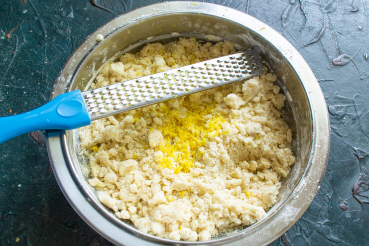 Adding fresh lemon zest for a bright flavor A hand grating fresh lemon zest directly into the cookie dough bowl.