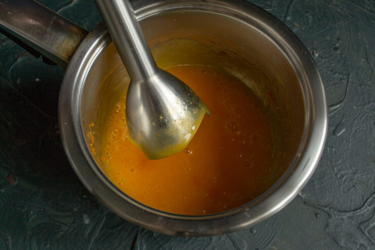 Blending the fruit sauce to a smooth consistency A hand blender pureeing the cooked fruit sauce until smooth.