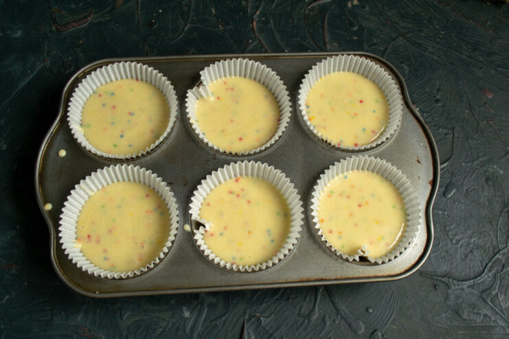 Step 7: Filling cupcake liners with batter Pouring confetti cupcake batter into paper liners in a muffin tin.