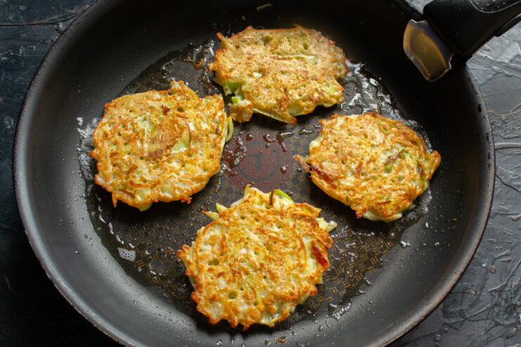 Cooking Draniki Until Crispy and Golden Brown Golden-brown draniki frying in a pan, being flipped with a spatula.