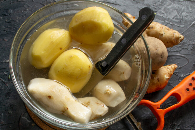 How to Peel Potatoes for Perfect Pancakes A hand holding a peeler and peeling a potato over a bowl.