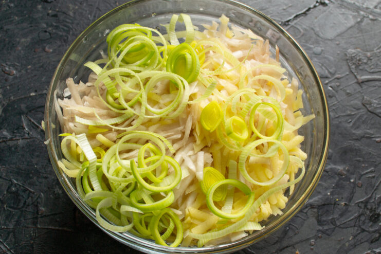 Adding Finely Chopped Leek to the Batter A bowl with grated vegetables, with finely chopped leek being added.