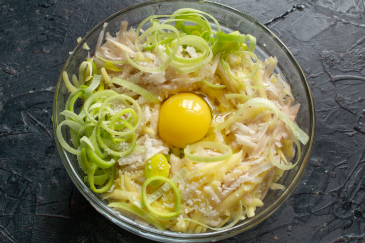Binding the Draniki Batter with Eggs Cracking eggs into a bowl of grated vegetables for the draniki batter.