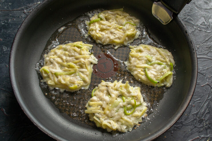 Frying the Draniki to Golden Perfection Spoonfuls of draniki batter being placed into a hot frying pan with oil.