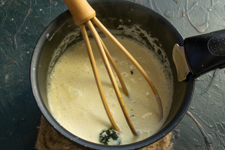 Chopped fresh basil being stirred into the creamy cheese sauce in a saucepan.