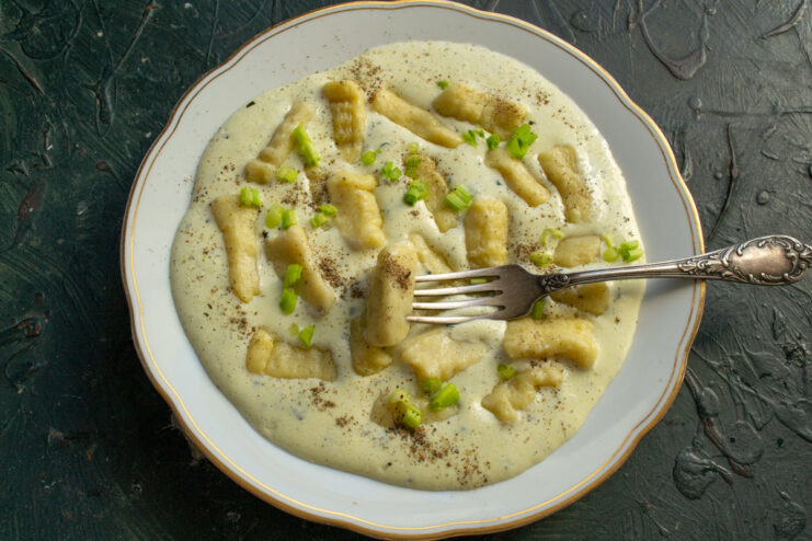 Cooked gnocchi being placed into a bowl with a creamy cheese sauce, ready to be served.