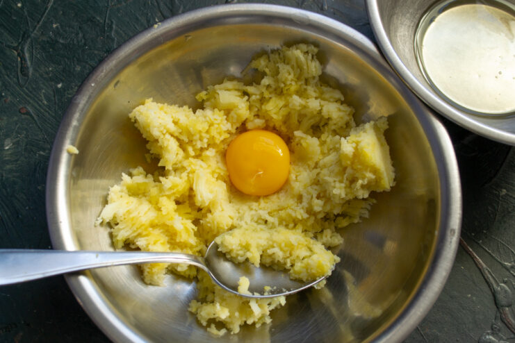 Egg yolks being added to a bowl of riced potatoes for making gnocchi dough.