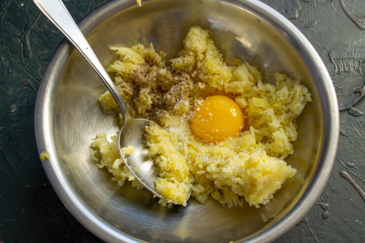 Salt and pepper being added to the potato and egg yolk mixture in a bowl.