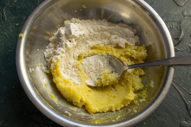Flour being added to the potato mixture in a bowl to form the gnocchi dough.